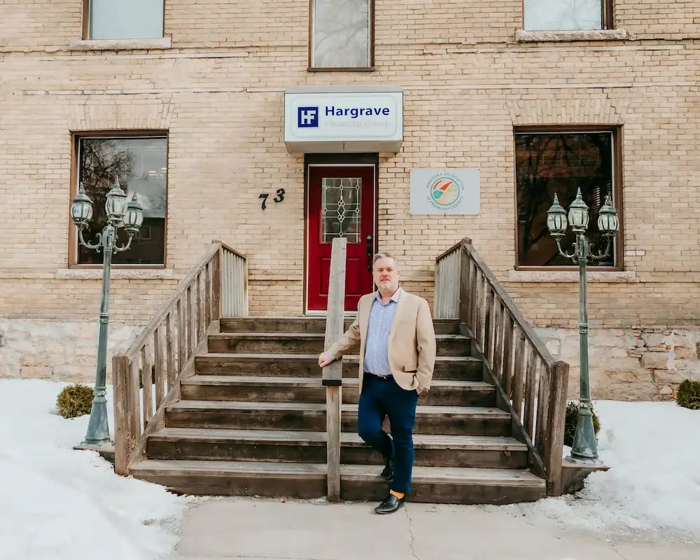 Morgan Kotz standing outside old brick character building with sign for Hargrave Financial Group.