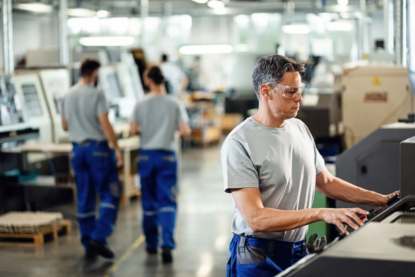 Man at a machine in a factory. Workers in the background.